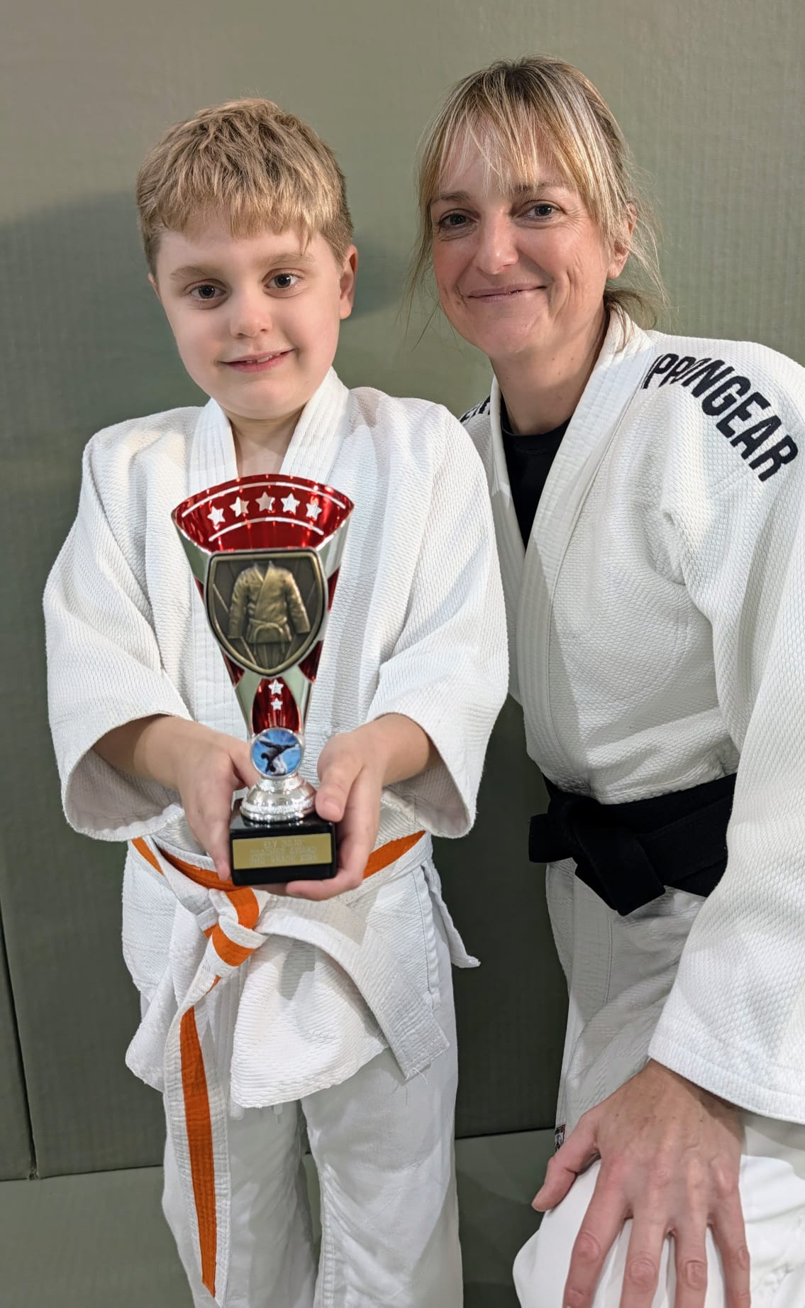 A young Ely Dojo member celebrating a trophy alongside a supportive coach